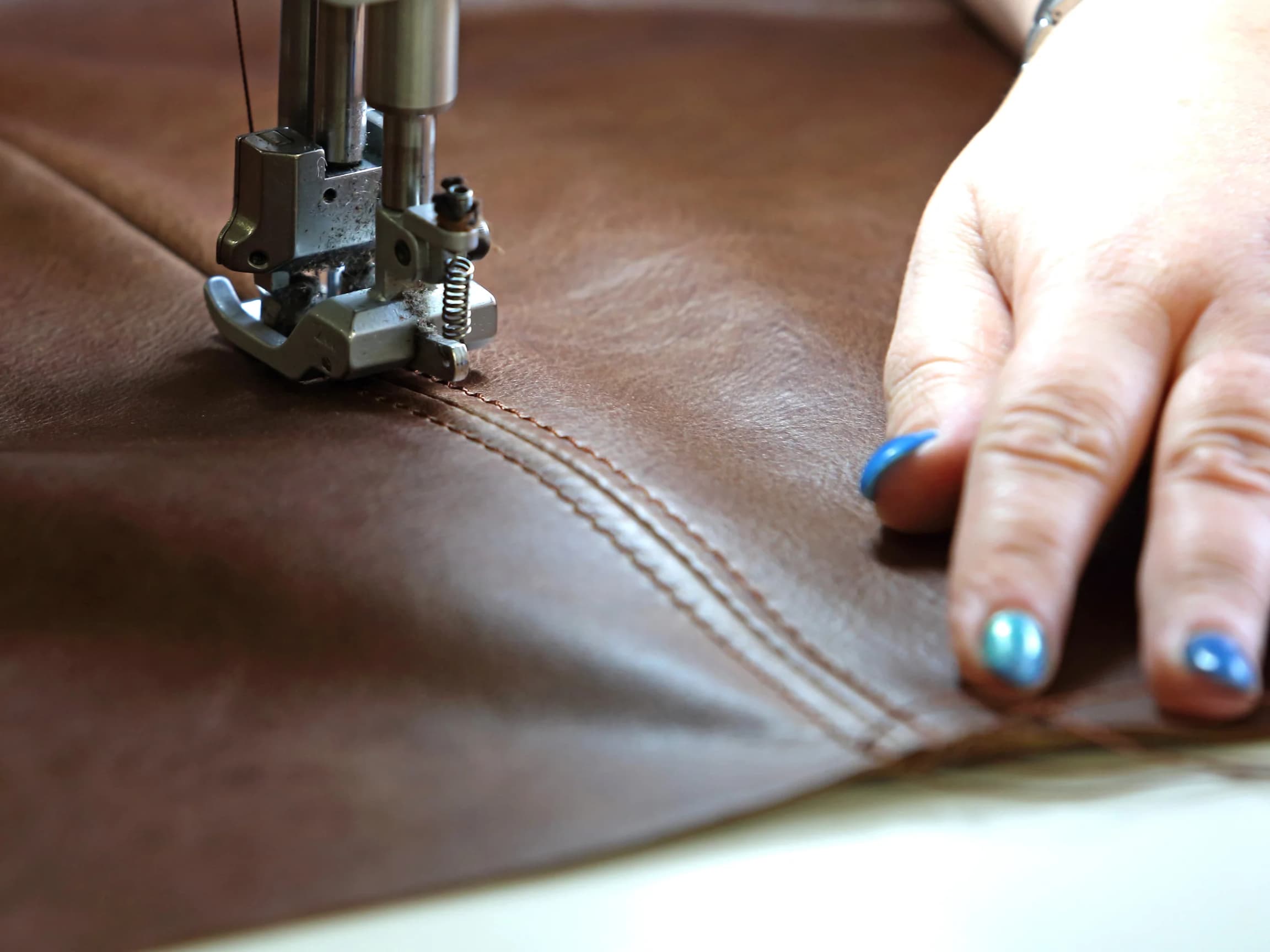A double row of stitching along a leather seam, freshly sewn under the presser foot of an industrial sewing machine.