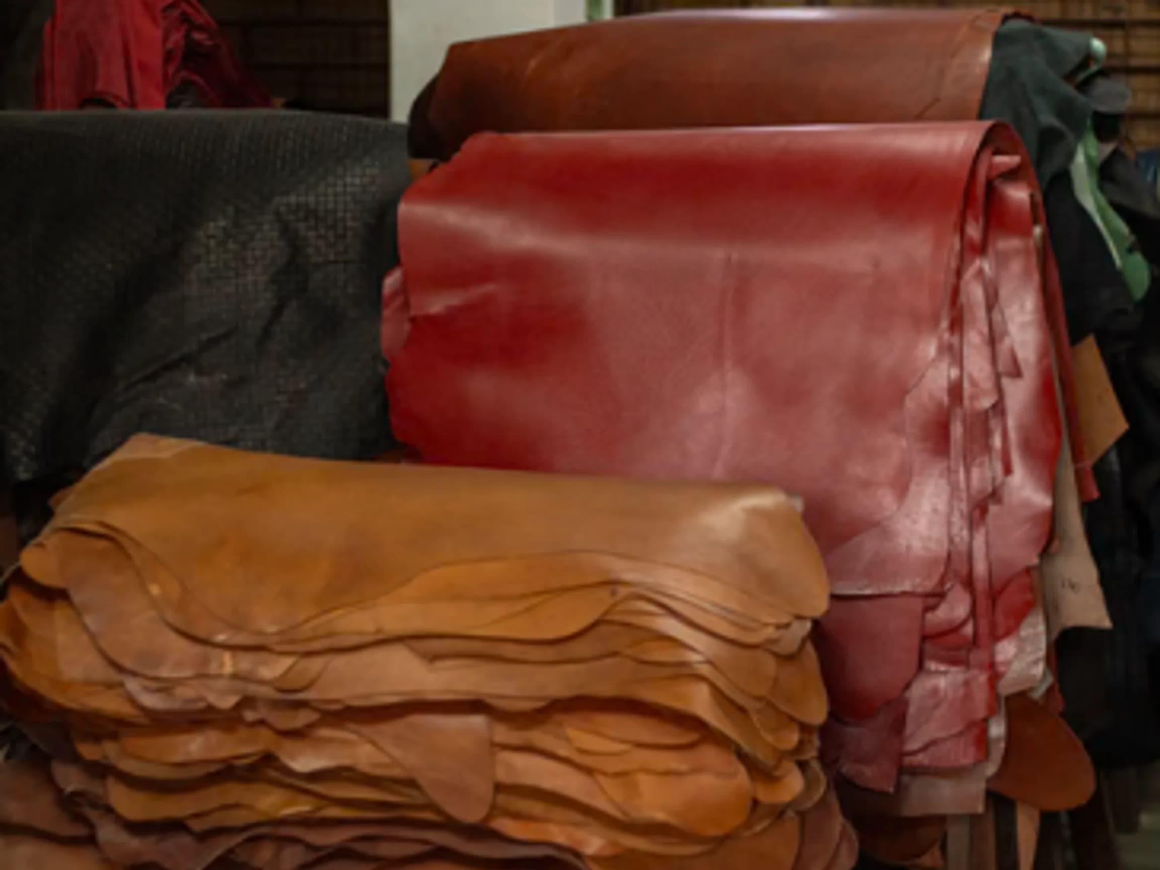 Stacks of aniline leather hides in tan, red and black, folded and rolled in the leather store before cutting.